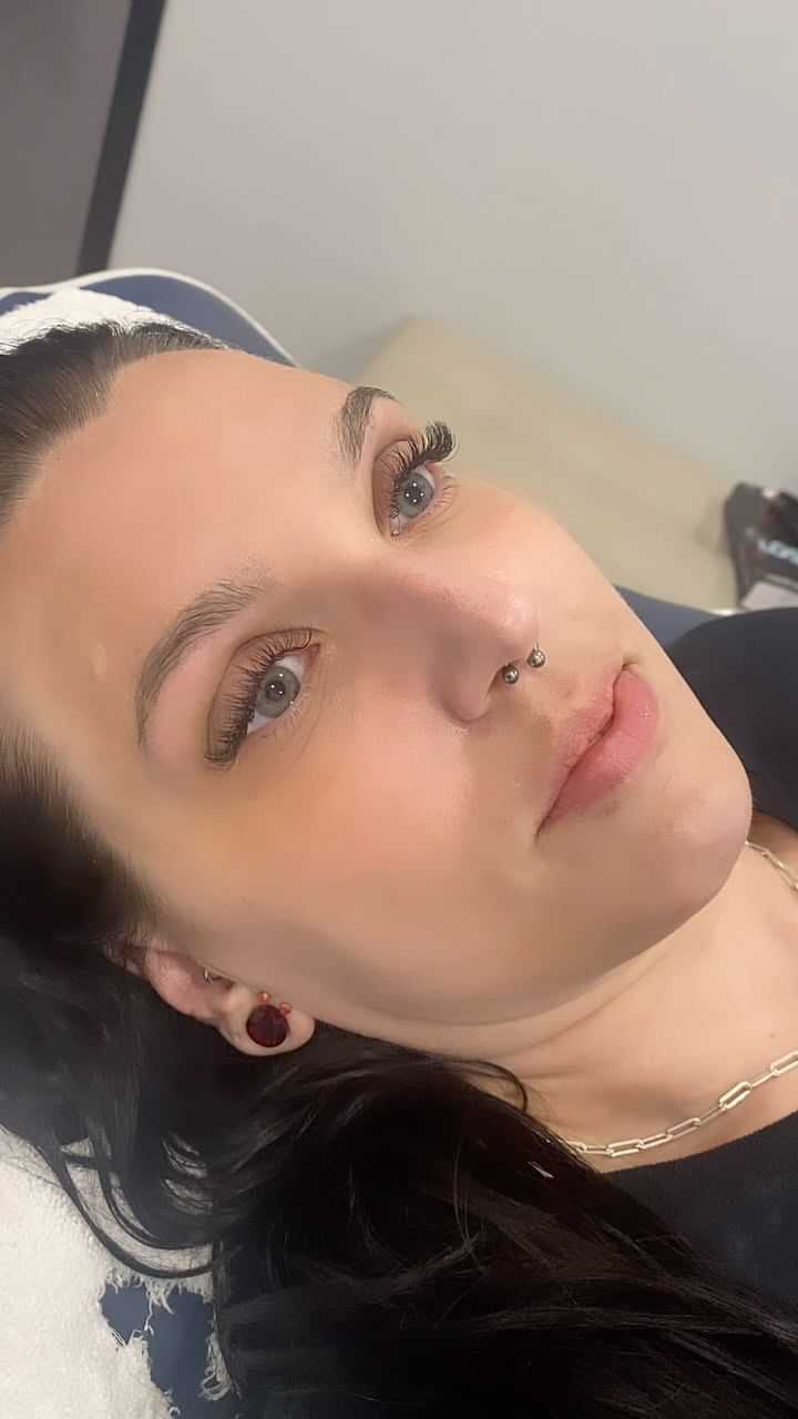 Woman with septum piercing relaxing on a couch, neutral expression, gaze upwards.