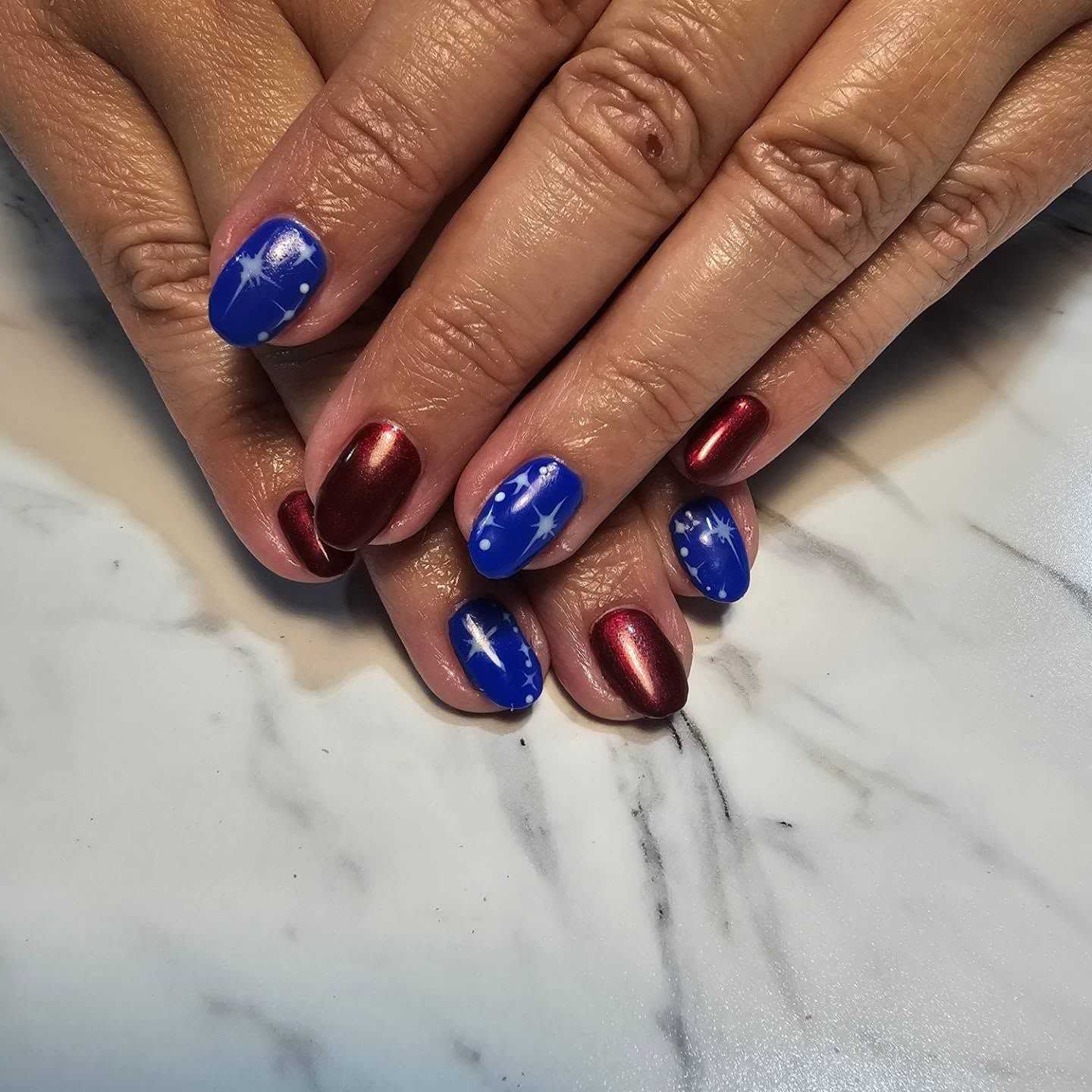 Red and blue nail art with white star designs on marble surface.