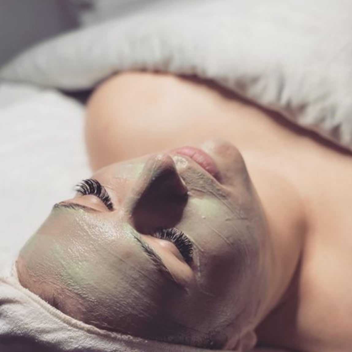 Facial mask application on a relaxed person with a towel head wrap.